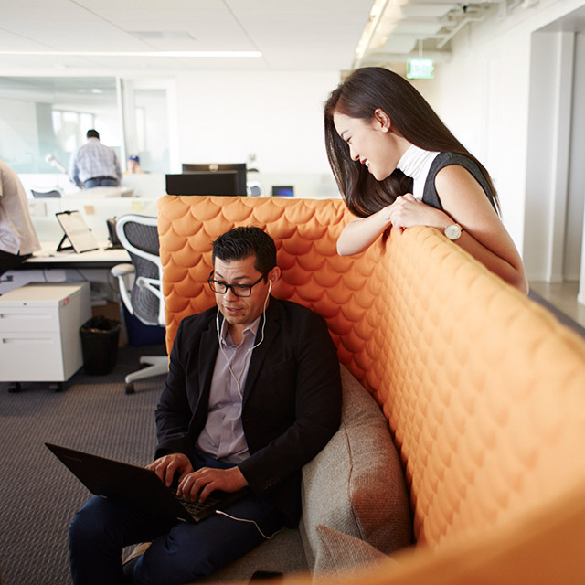 Man with a laptop sitting on a couch while a woman looks over him.