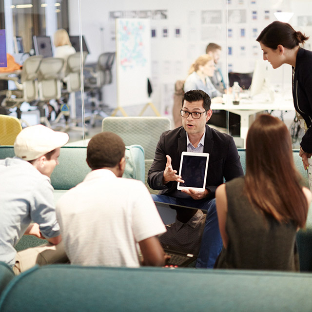 Man holding a tablet while talking to an audience.