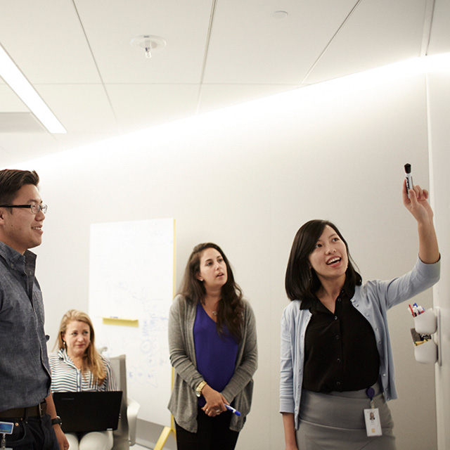 Woman gesturing with a marker while three people look at her.