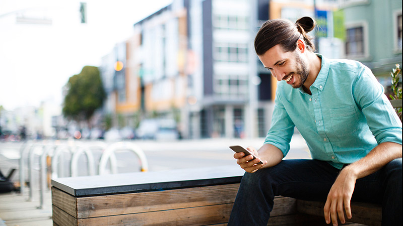 Seated man using smart phone in a city setting.
